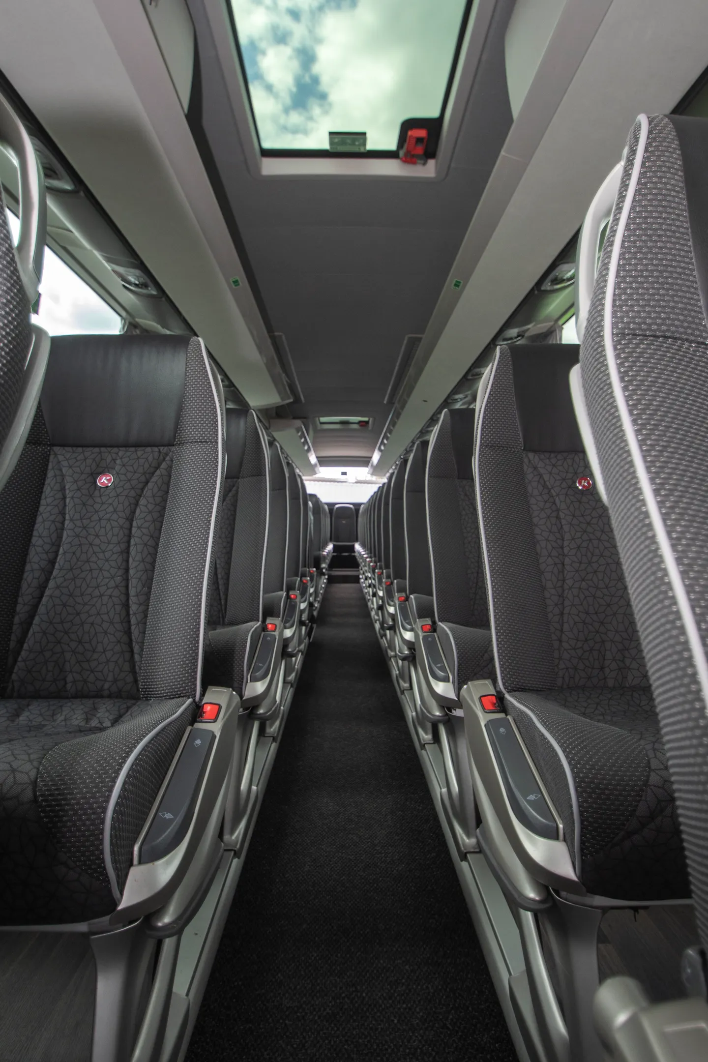 Innenraum eines Reisebusses mit Sitzreihen, Mittelgang und Dachluke